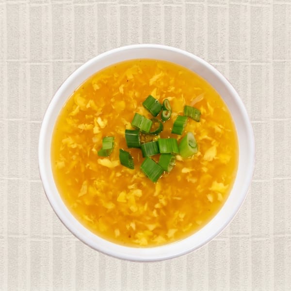 Overhead view of a white bowl filled with golden egg drop soup, garnished with chopped green onions.