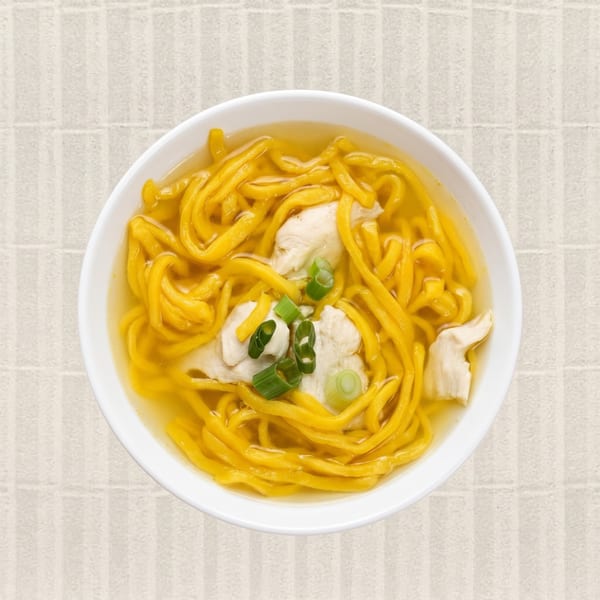 Overhead view of a white bowl filled with yellow noodles, chicken, and green onions in broth.