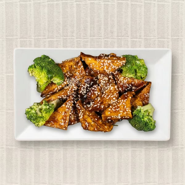 Sesame-crusted tofu triangles with a glossy brown sauce and green broccoli florets on a white rectangular plate.