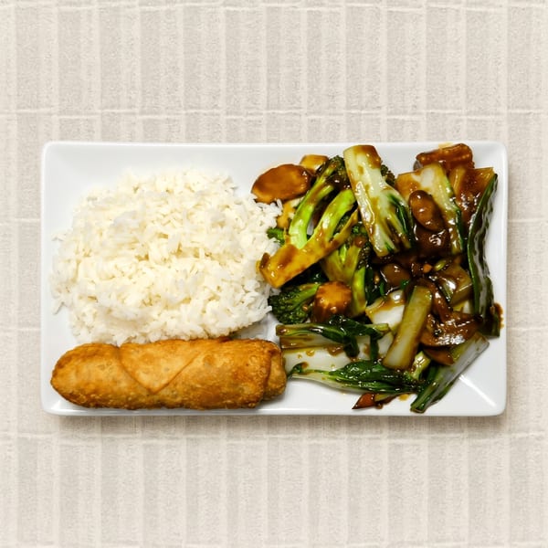 A white rectangular plate with white rice, stir-fried vegetables in sauce, and a golden-brown egg roll.