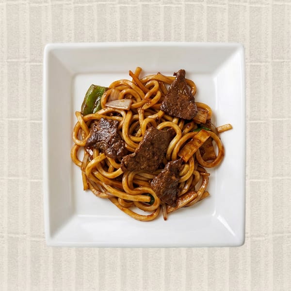 Beef Udon Noodles with green peppers and onions in a white square bowl.