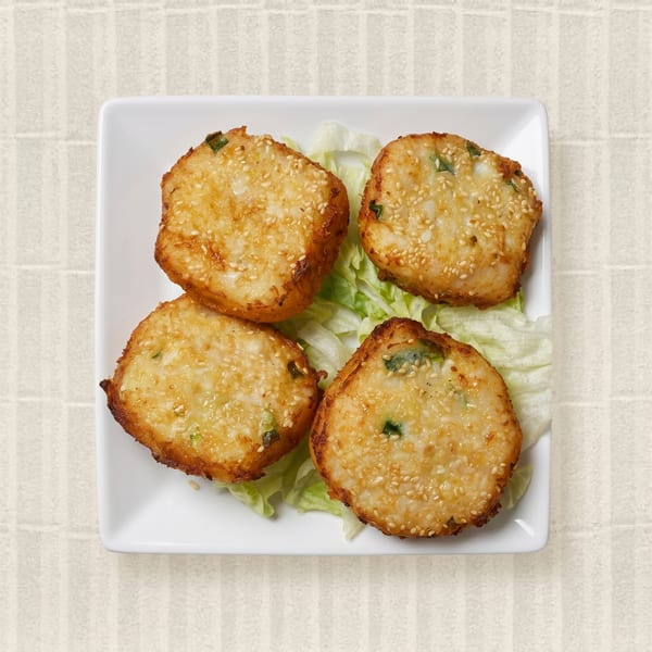 Four golden-brown sesame shrimp toasts with green onions, served on lettuce on a white plate.